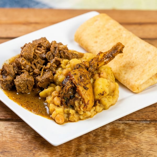 A white plate with stewed meat, chicken, chickpeas, potatoes, and a folded flatbread.