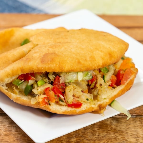 Fried bake and saltfish, filled with colorful vegetables, on a white plate atop a wooden table.