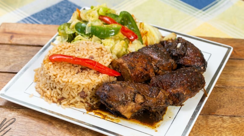 A plate of brown stew chicken, rice and peas, and steamed cabbage with red peppers.