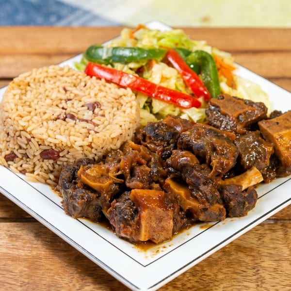 A plate of oxtail stew with rice and peas, and steamed cabbage with peppers.