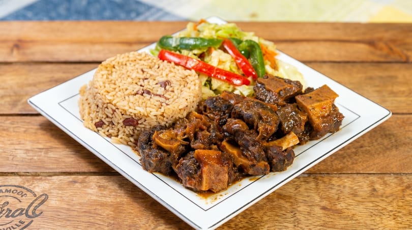 A plate of oxtail stew with rice and peas, and steamed cabbage with peppers.