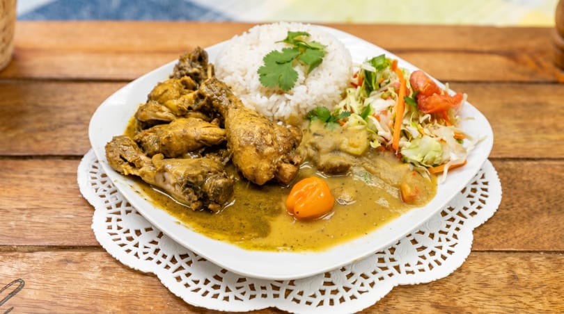 Curried chicken with rice, salad, and a whole habanero pepper on a white plate.